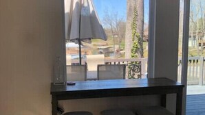 Habitación con ventana que da a una terraza, una mesa pequeña con una silla y un enchufe en la pared.
