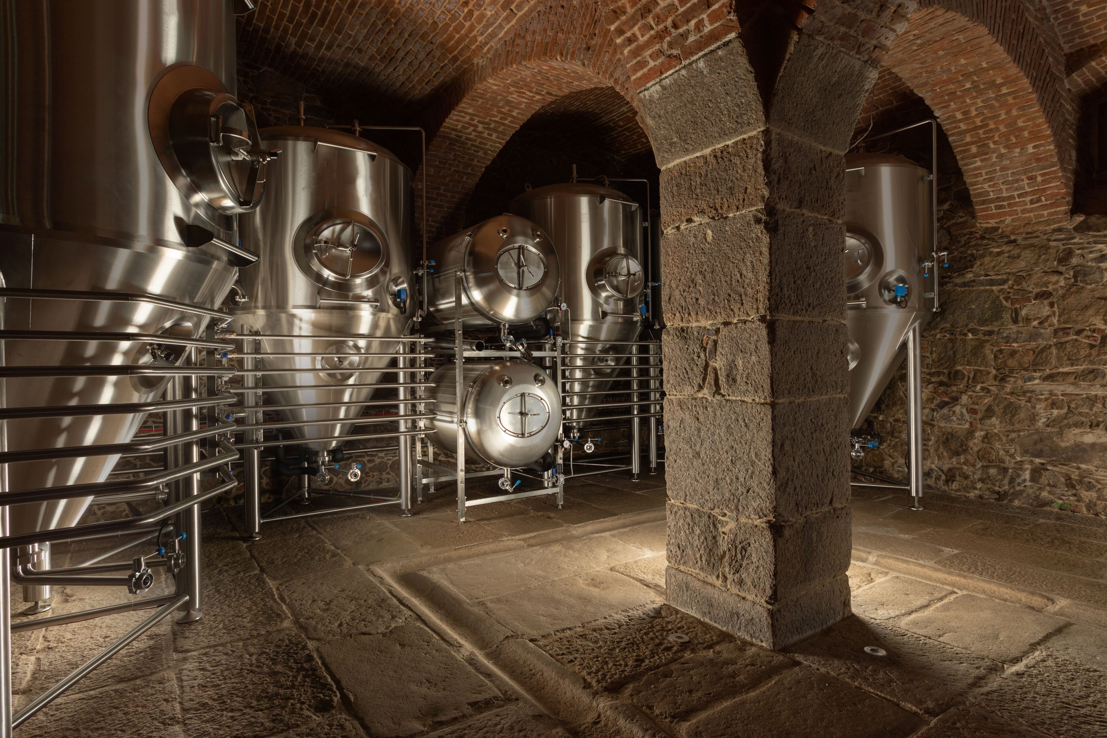 Cuves de brassage en acier inoxydable, installées dans une cave aux murs de pierre et aux voûtes en arc.