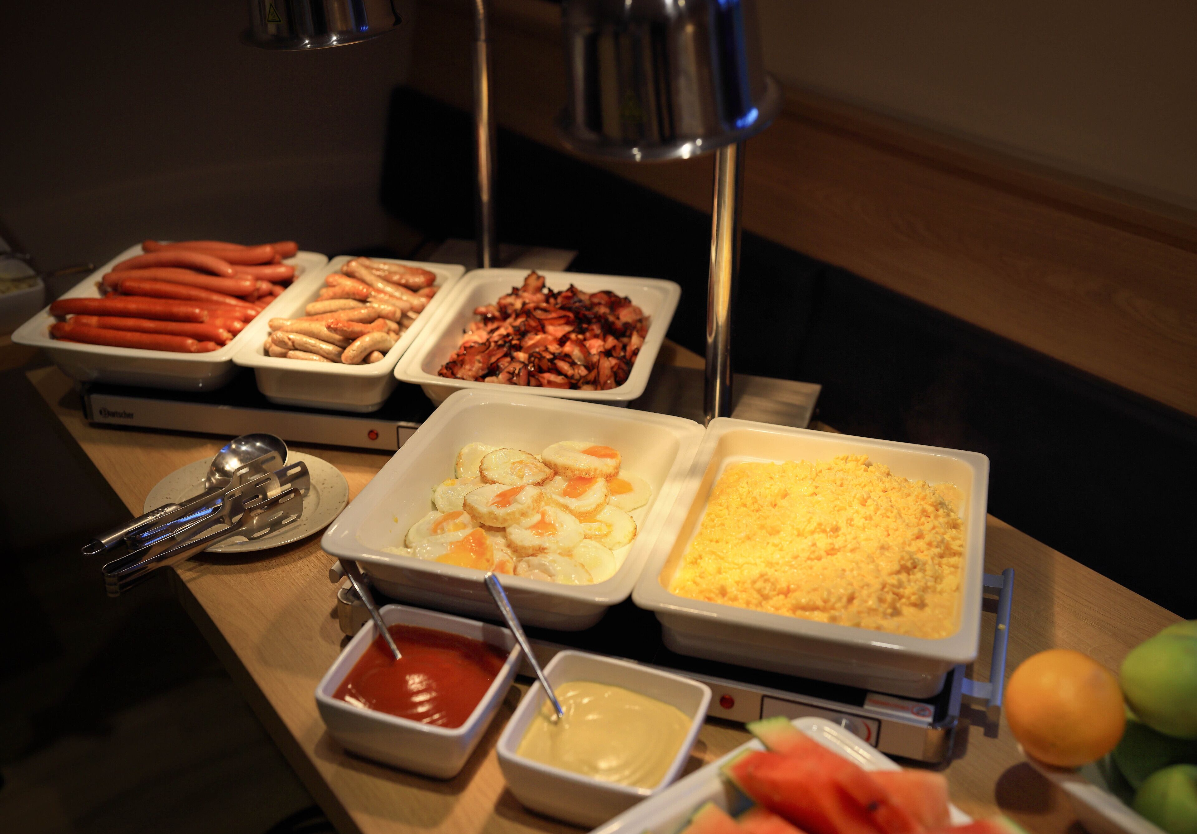 Una mesa de buffet con diversos alimentos, incluyendo hot dogs, camarones y un plato de cazuela.