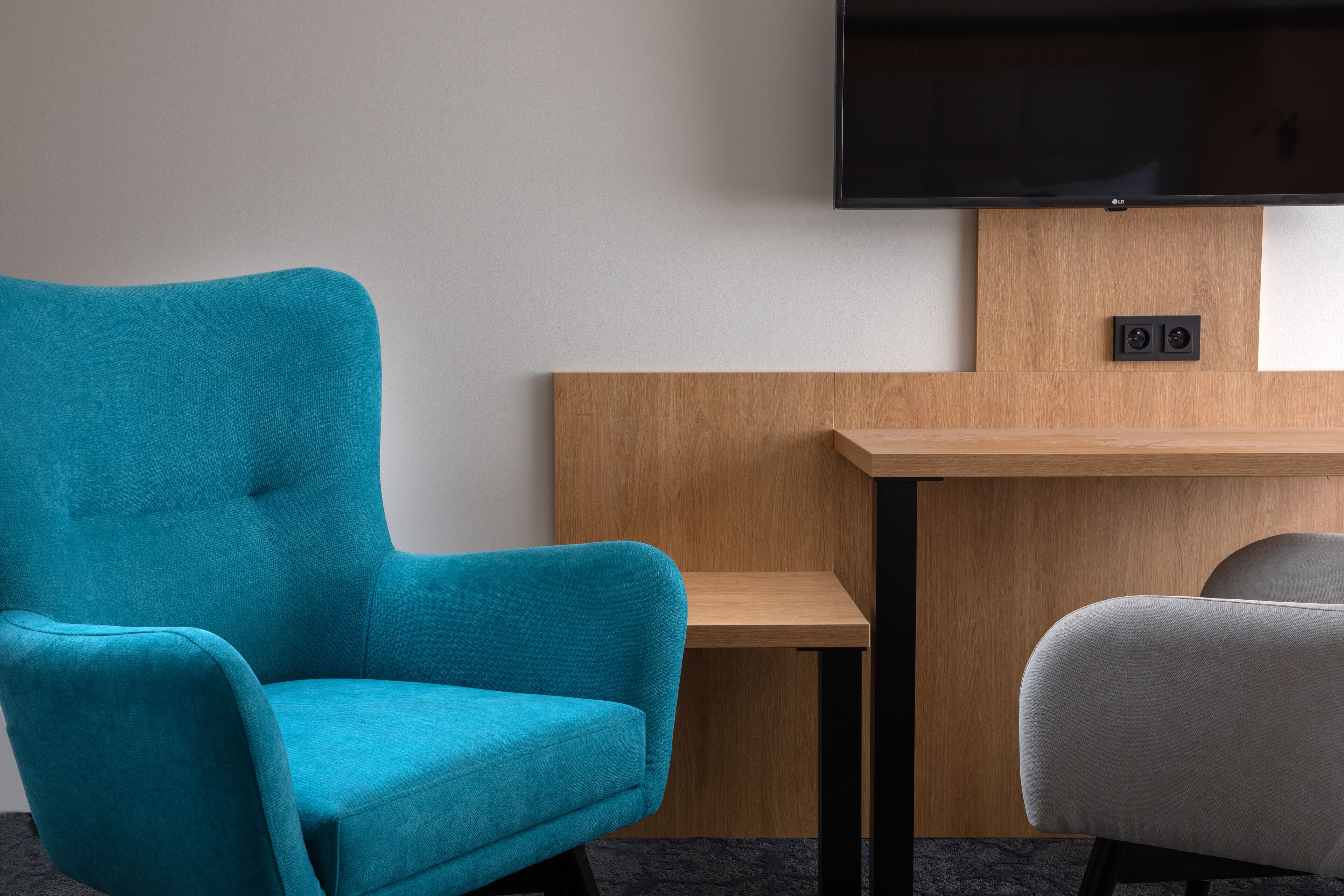 Un sillón azul turquesa, una silla gris y un escritorio de madera con un televisor de pantalla plana montado encima.