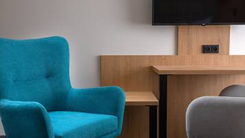 Un sillón azul turquesa, una silla gris y un escritorio de madera con un televisor de pantalla plana montado encima.