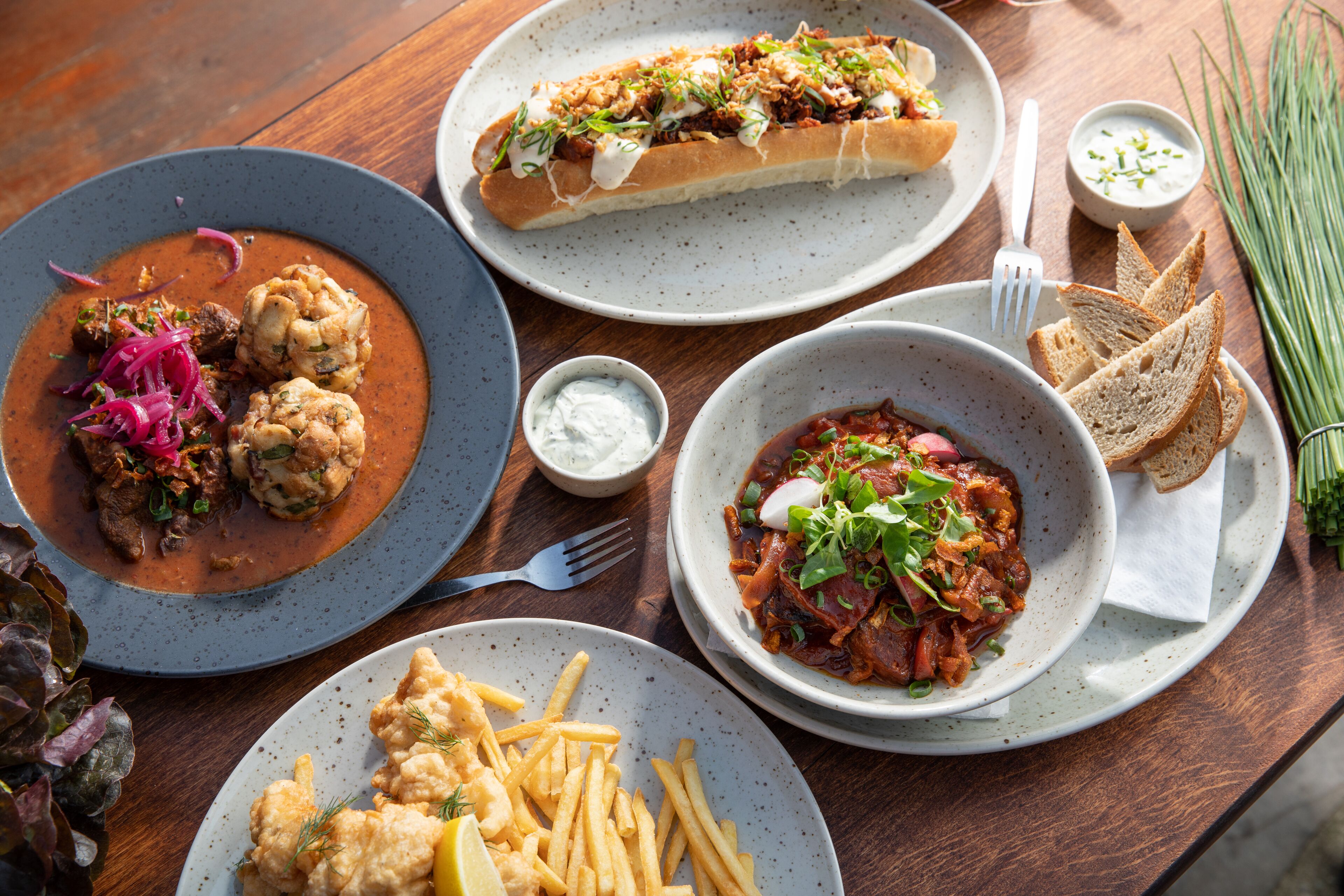 A variety of dishes including a fish dish with lemon, a meat dish with sauce, a bread roll with toppings, and a bowl of salad.