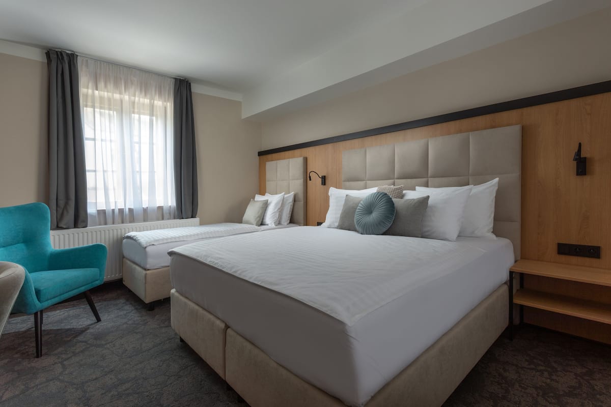 A hotel room with a large bed, a bedside table, a chair, and a window with curtains.