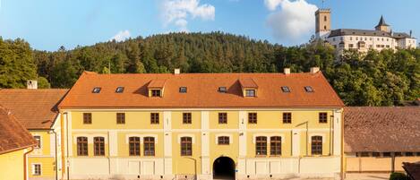 A large, yellow building with a red-tiled roof, a central entrance, and a small archway.