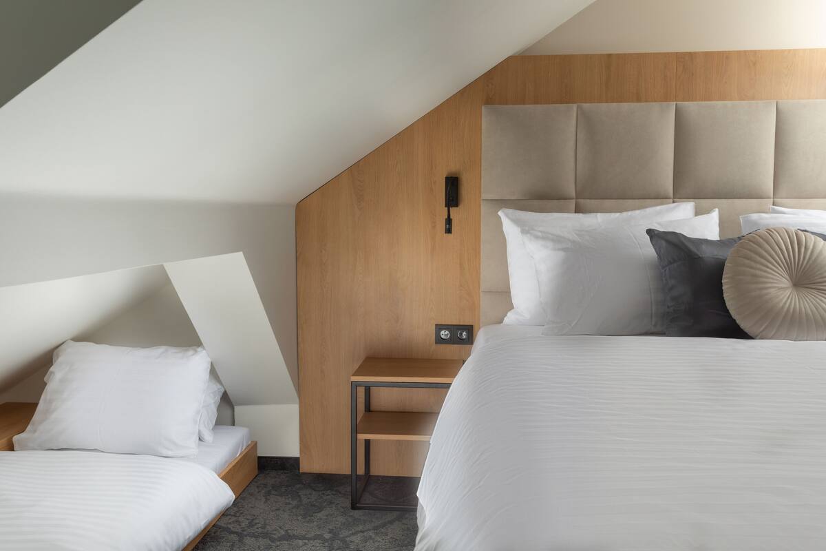 A modern hotel room with a sloped ceiling, a wooden headboard, and a small bedside table.