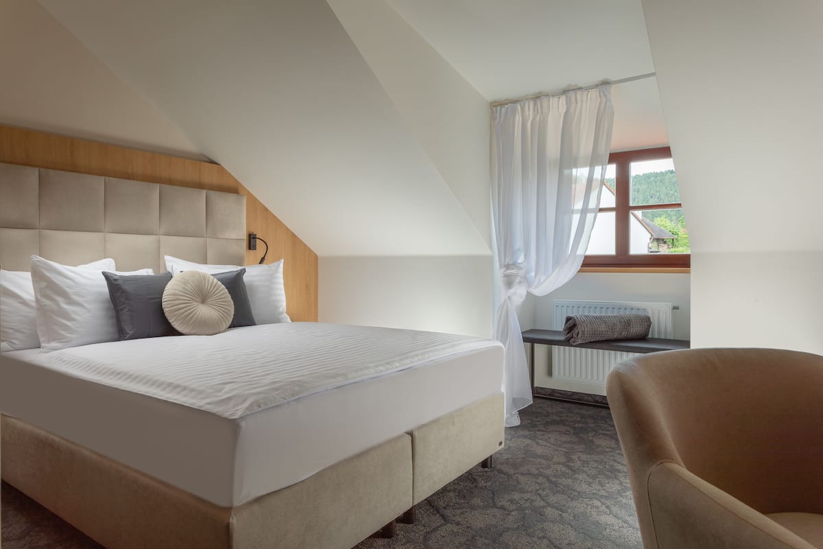 A bedroom with a large bed, a wooden headboard, a window with a view of greenery, and a chair.