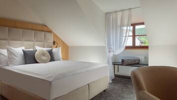Quarto com uma cama grande, cabeceira de madeira, janela com vista para área verde e uma cadeira.