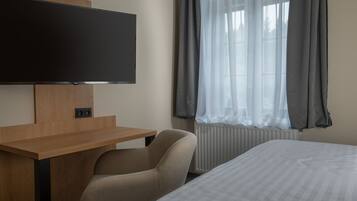Une chambre d’hôtel comprenant un lit, un bureau avec un téléviseur à écran plat, une chaise et une fenêtre avec des rideaux.