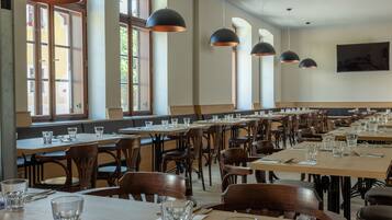 A spacious dining area with multiple tables and chairs, large windows, and pendant lighting.