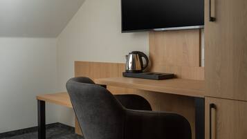 Une chambre moderne avec un bureau en bois, deux chaises noires, un téléviseur à écran plat fixé au mur et une machine à café posée sur le bureau.