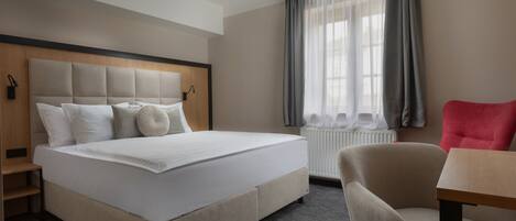 A hotel room with a large bed, a chair, a table, and a window with curtains.