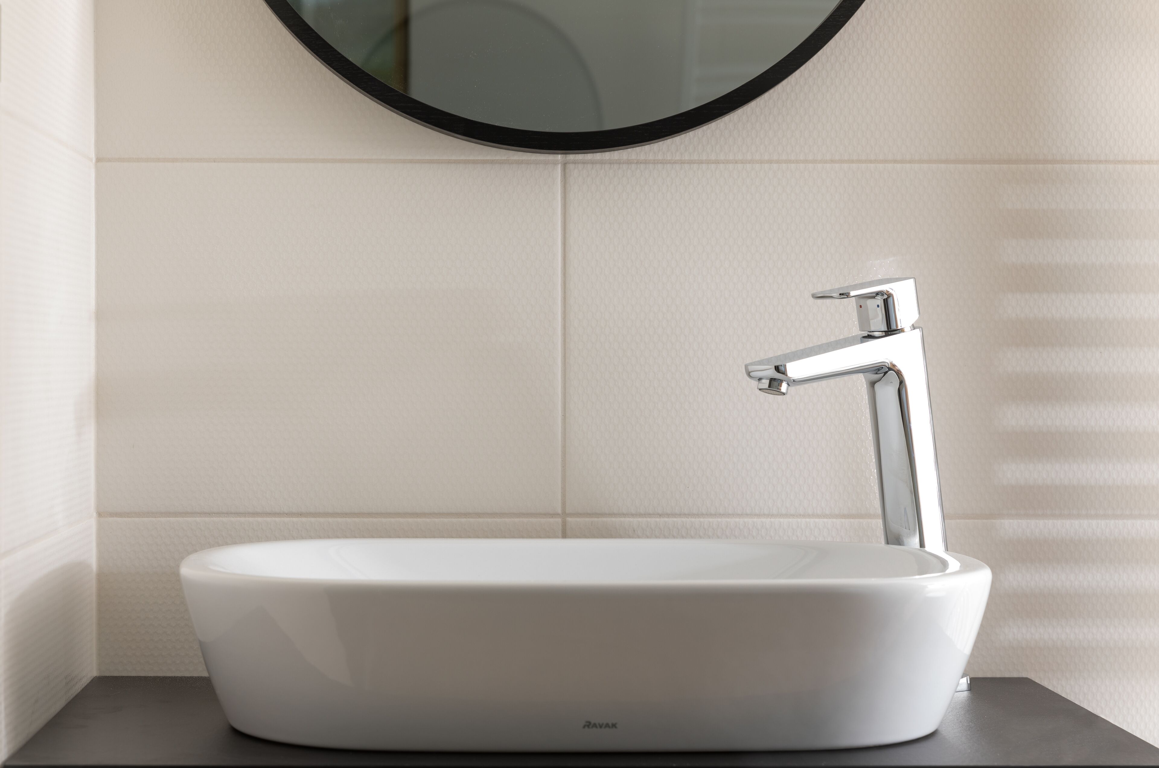 Un baño moderno con un lavamanos blanco, grifo cromado y un espejo redondo encima.