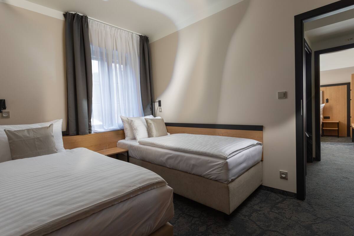 A hotel room with two beds, a large window with sheer curtains, a wooden headboard, and a carpeted floor.
