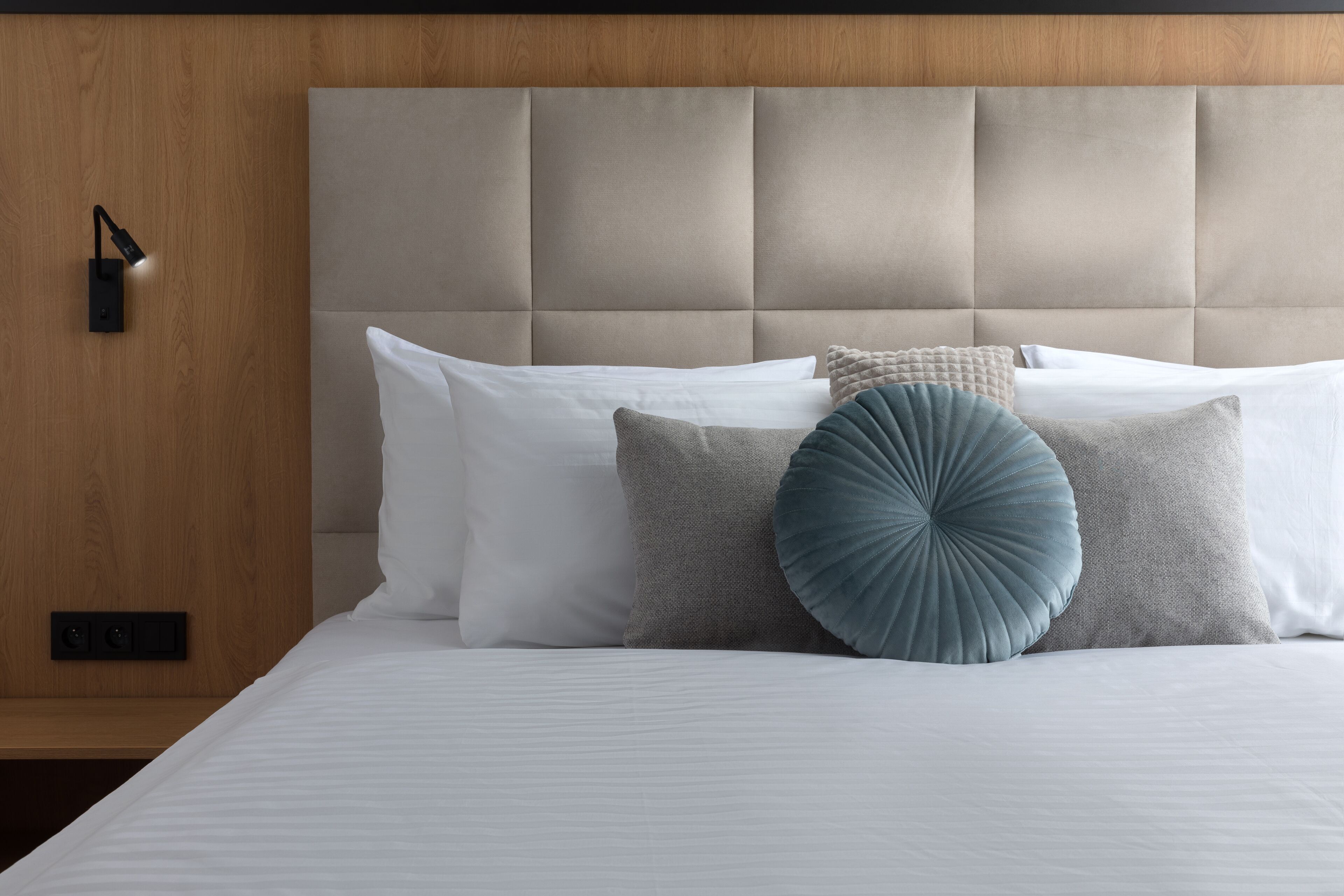 A neatly made bed with a tufted headboard, white and grey pillows, and a blue accent pillow.