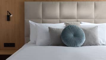 Un lit bien fait, avec une tête de lit capitonnée, des oreillers blancs et gris, et un coussin bleu qui apporte une touche de couleur.