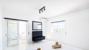 A modern bedroom with a large bed, a dark sofa, a mirror, and a view of the city. - Spacious Villa: Jacuzzi, Cinema & Heatable Pool (Pêra)