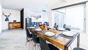 A modern dining area with a wooden table set for four, a kitchen in the background, and a large window providing a view. - Spacious Villa: Jacuzzi, Cinema & Heatable Pool (Pêra)