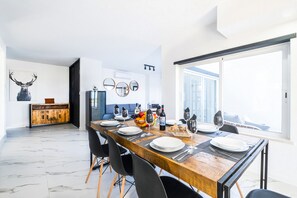 A modern dining area with a wooden table set for four, a kitchen in the background, and a large window providing a view. - Spacious Villa: Jacuzzi, Cinema & Heatable Pool (Pêra)