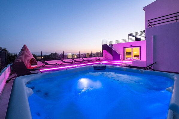 A rooftop swimming pool with a hot tub, lounge chairs, and a pink-lit deck area.