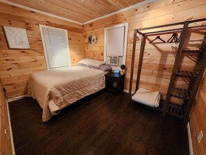 Cozy cabin with a bed, bedside table, and air conditioning unit, featuring a loft-style storage area and a framed picture on the wall.