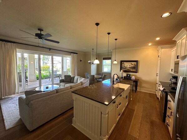 A modern kitchen with a central island, a dining area with a sofa, and a view of the outdoors through large sliding doors.
