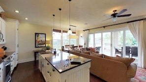 Amplia sala de estar con isla de cocina, comedor y balcón con mobiliario exterior.