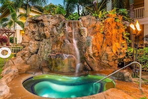 Un bain à remous entouré d’une cascade artificielle aux rochers, avec une piscine et une bouée de sauvetage visibles.