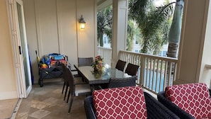 Un patio cubierto con una mesa y sillas, un sofá de mimbre y un carrito pequeño con equipo de ejercicio.