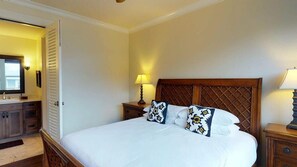 Quarto de hotel com uma cama grande, cabeceira de madeira, duas mesas de cabeceira com luminárias, um criado-mudo e um guarda-roupa.