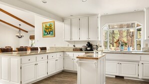 Una cocina amplia con armarios blancos, una isla grande y vista a árboles por una ventana.