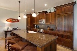 A kitchen with granite countertops, wooden cabinets, a stainless steel microwave, and a large island with bar stools.