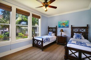 A bedroom with two wooden beds, a ceiling fan, and large windows with views of greenery.