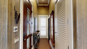 Un pasillo con una puerta de madera, un letrero de bienvenida, un banco y una puerta con persianas horizontales.