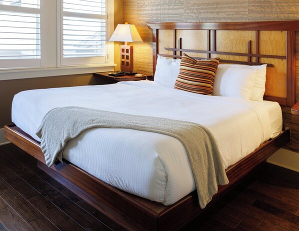 A large bed with a wooden headboard, white bedding, and a bedside table with a lamp.