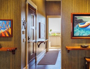 A hallway with wooden doors, a doormat, and framed artwork on the walls.