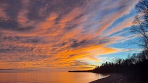 A sunset over a calm lake with a shoreline and trees.