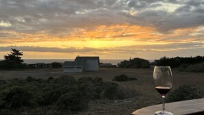 Vista al atardecer desde un balcón, con una copa de vino, que da a un campo cubierto de hierba y un edificio distante.