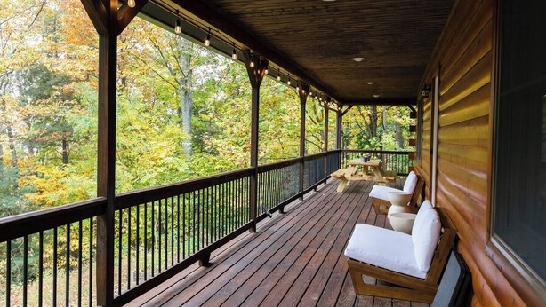 Una terraza de madera con barandilla, un banco y una mesa, con vistas a un área boscosa.