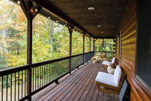 A wooden deck with a railing, a bench, and a table, overlooking a forested area.