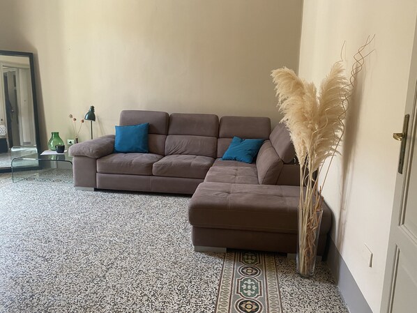 A living room with a brown sectional sofa, a patterned rug, and a tall vase with pampas grass. - Cavour Apartments by Wonderful Italy (Noto)
