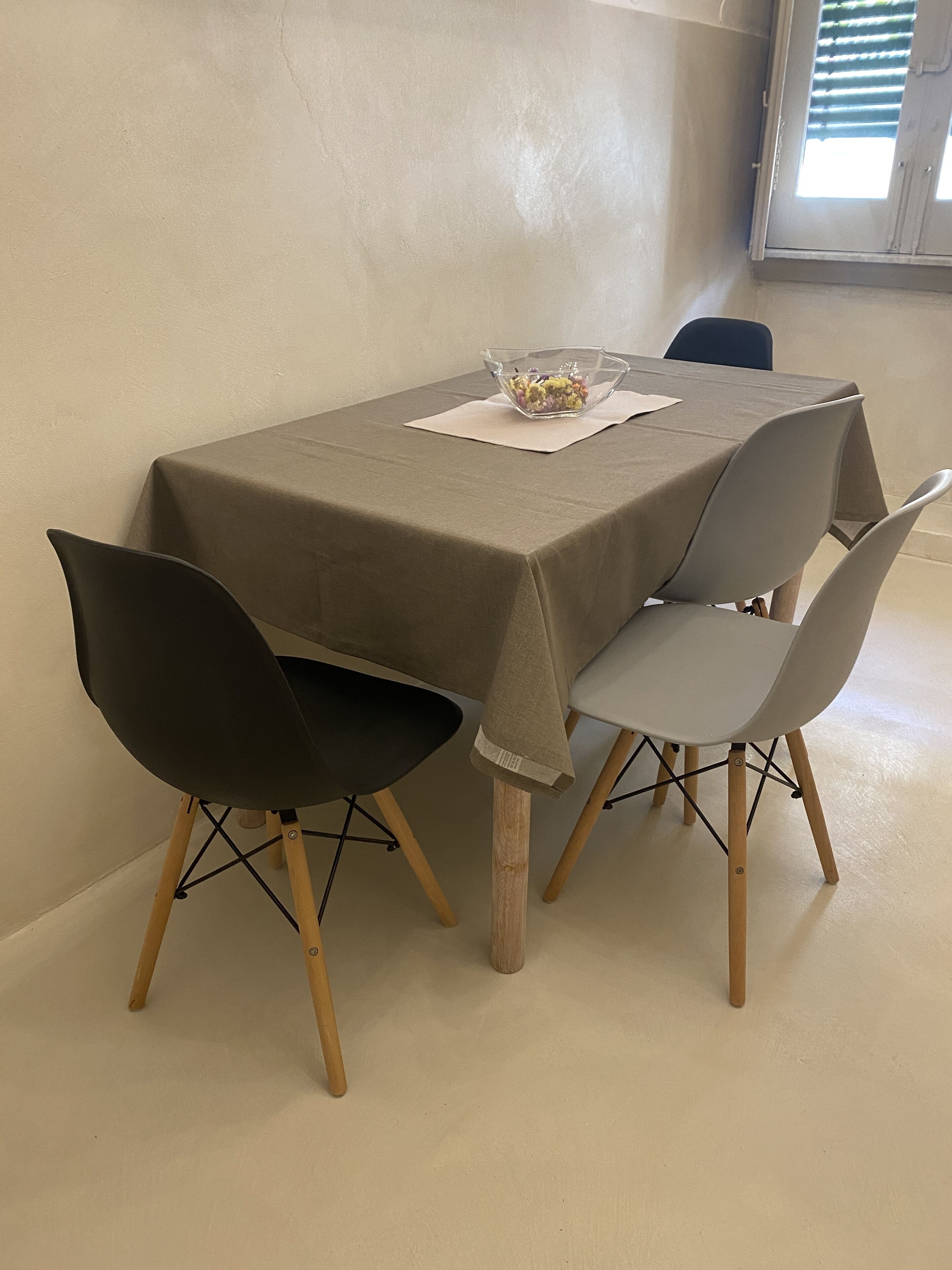 A dining table with a beige tablecloth, surrounded by four chairs with wooden legs and grey upholstery.