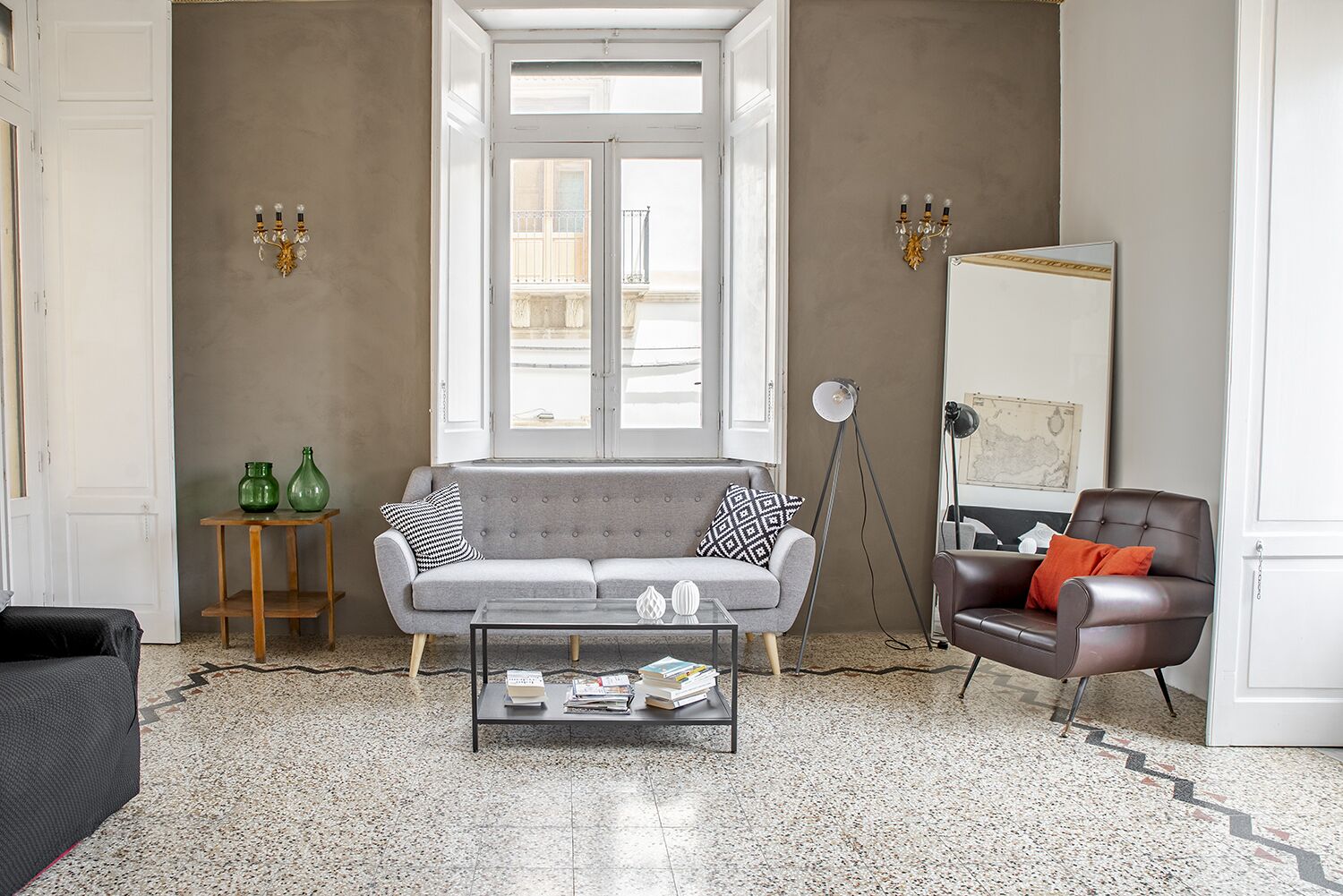 A living room with a grey sofa, a coffee table with books, a floor lamp, and a brown leather armchair.