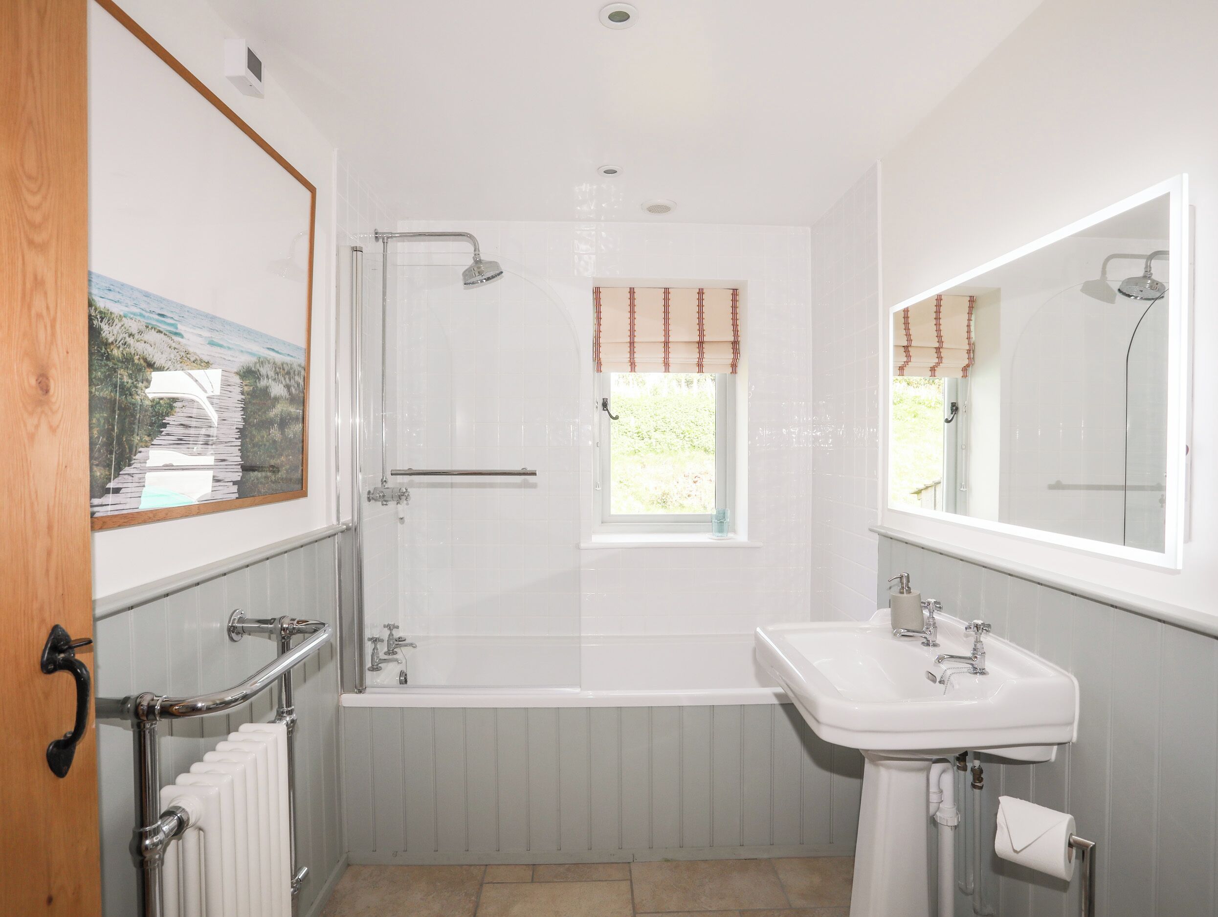 Een badkamer met een bad, een wastafel, een raam met gordijnen, een radiator en een houten deur.