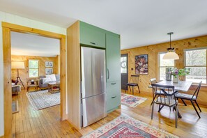 A spacious living area with a large wooden dining table, a green kitchen with a stainless steel refrigerator, and a cozy seating area with a sofa and armchairs. - Gorgeous Sunday River Cabin w/ Saltwater Hot Tub! (Hanover)