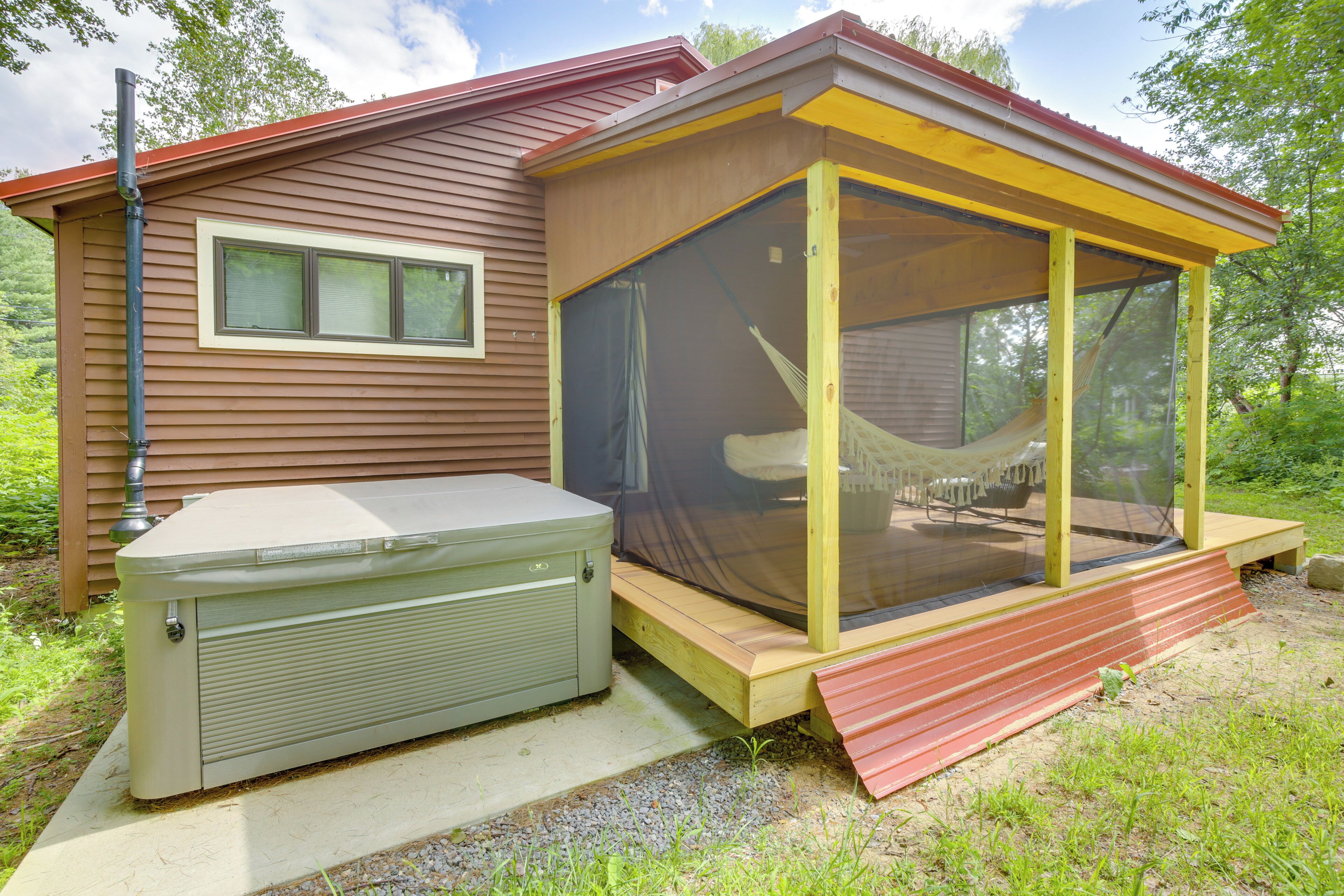 Een klein huis met een overdekt terras en een hottub.