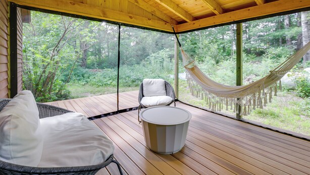 Un ponte in legno con mobili in vimini, un'amaca e vista su una foresta.