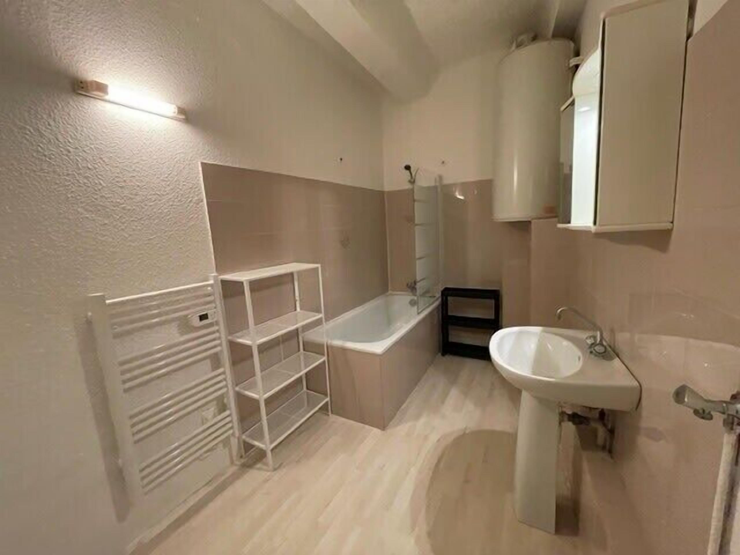 A bathroom with a bathtub, a sink, and a mirror. There is a shelf unit against the wall and a towel rack.