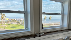 A dining area with two windows overlooking a beach and amusement park.