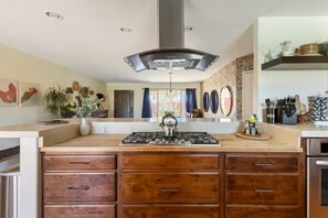 Une cuisine dotée d’un îlot central, de meubles en bois, d’une cuisinière à gaz et d’une hotte en acier inoxydable.