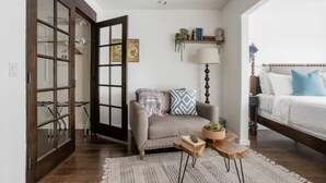 A cozy living room with a grey sofa, a small wooden coffee table, a lamp, and a bed with a wooden headboard. - Casa Bermuda a Spanish Boho Retreat, Expansive Pool/Spa Pet Friendly (Bermuda Dunes)